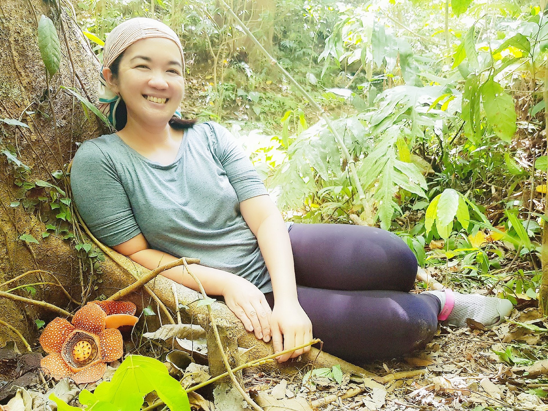Filipino scientist Dr. Aimee Dupo sitting at the roots of a giant tree with a couple of Rafflesia flowers