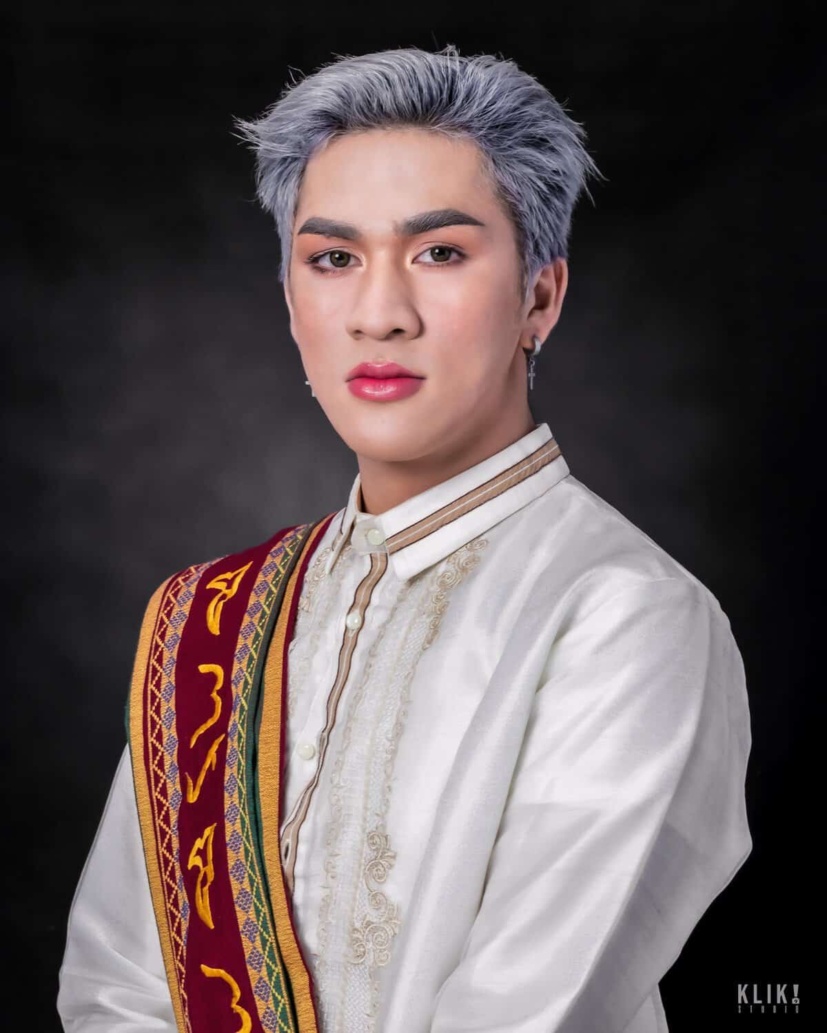 Rene Principe Jr. is wearing sablay (UP's official academic costume) over their barong. Their hair is dyed ash gray.