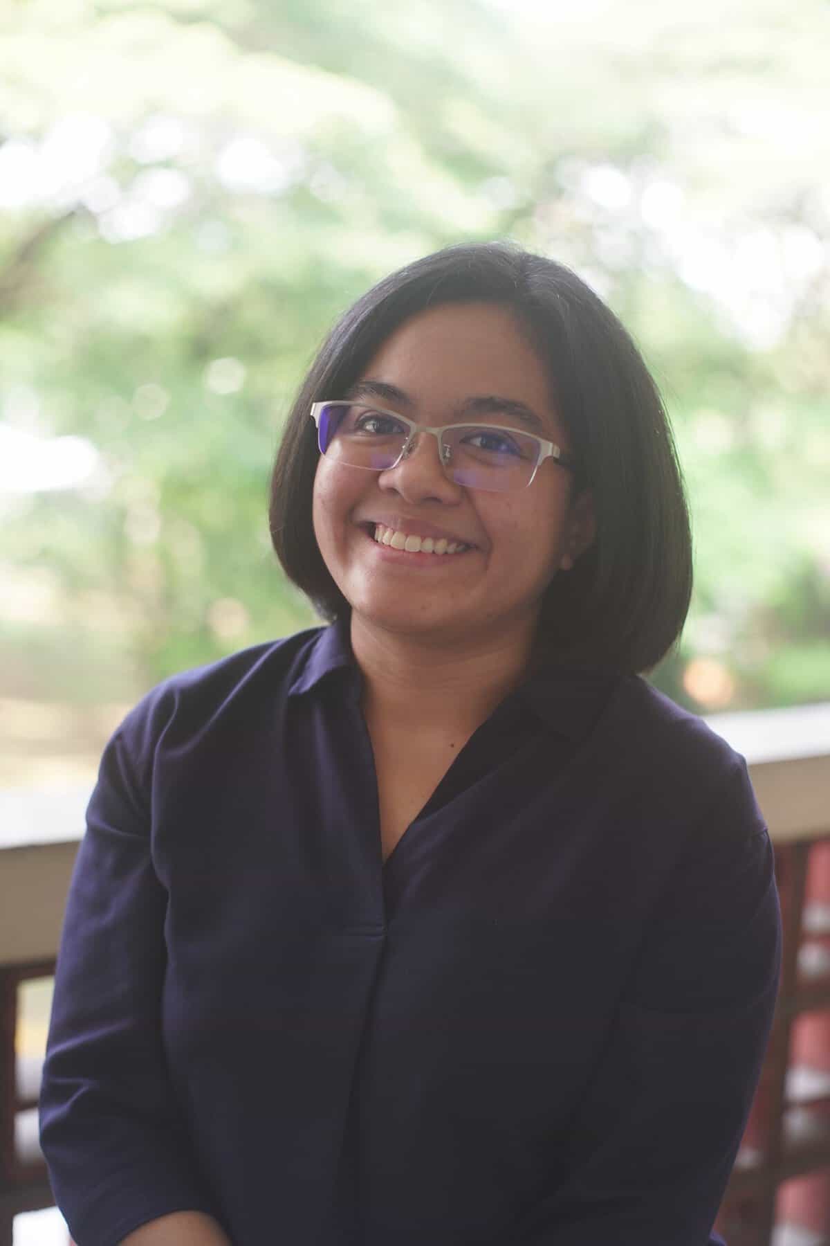 Pinoy scientist Janina Castro has shoulder-length hair and glasses. She is wearing a dark shirt, and the mood is cheerful and relaxed.