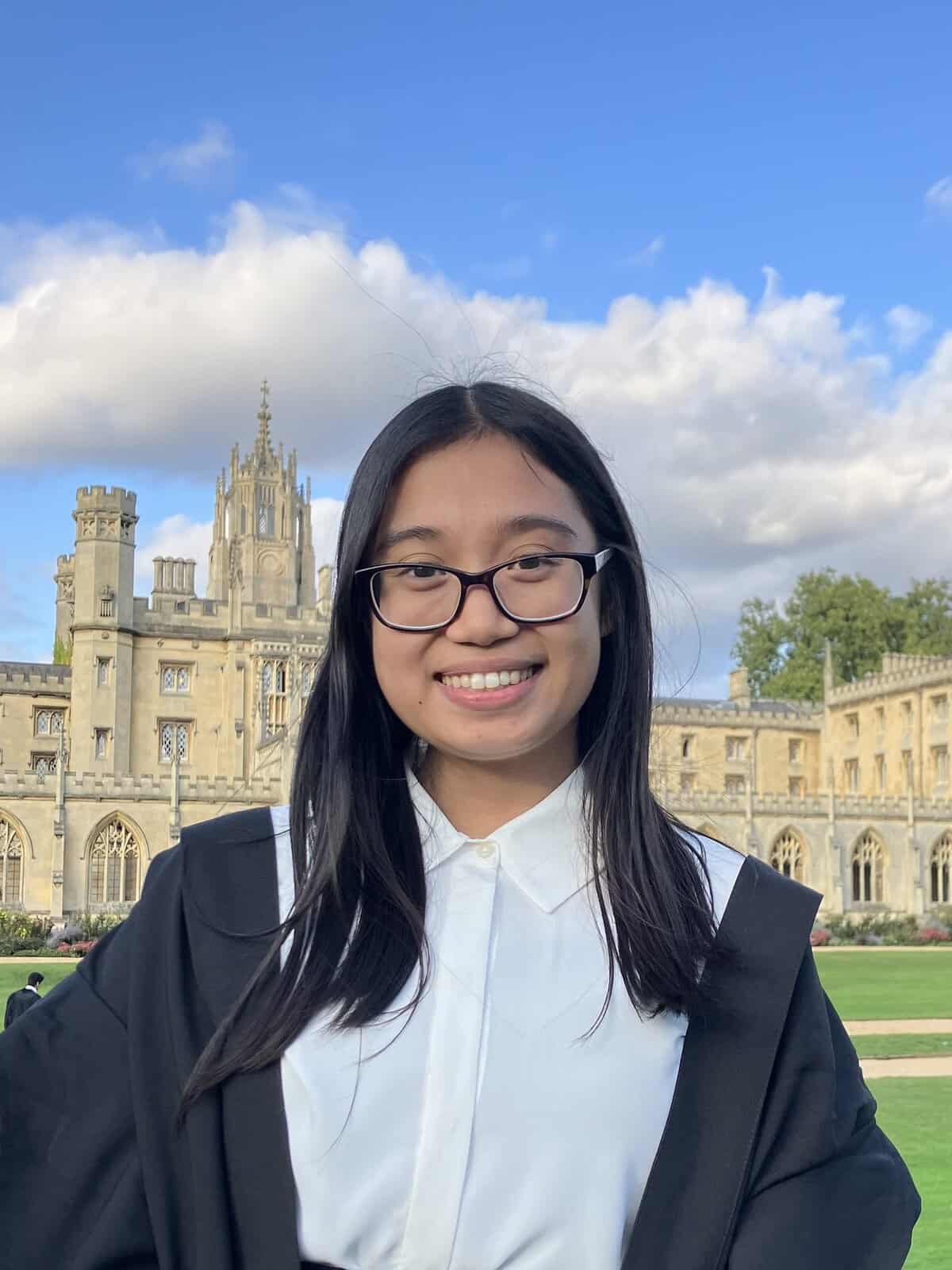 Pinoy Scientist Princess Buma-at is wearing glasses and a graduation gown. She stands in front of a historic stone building with a large tower.
