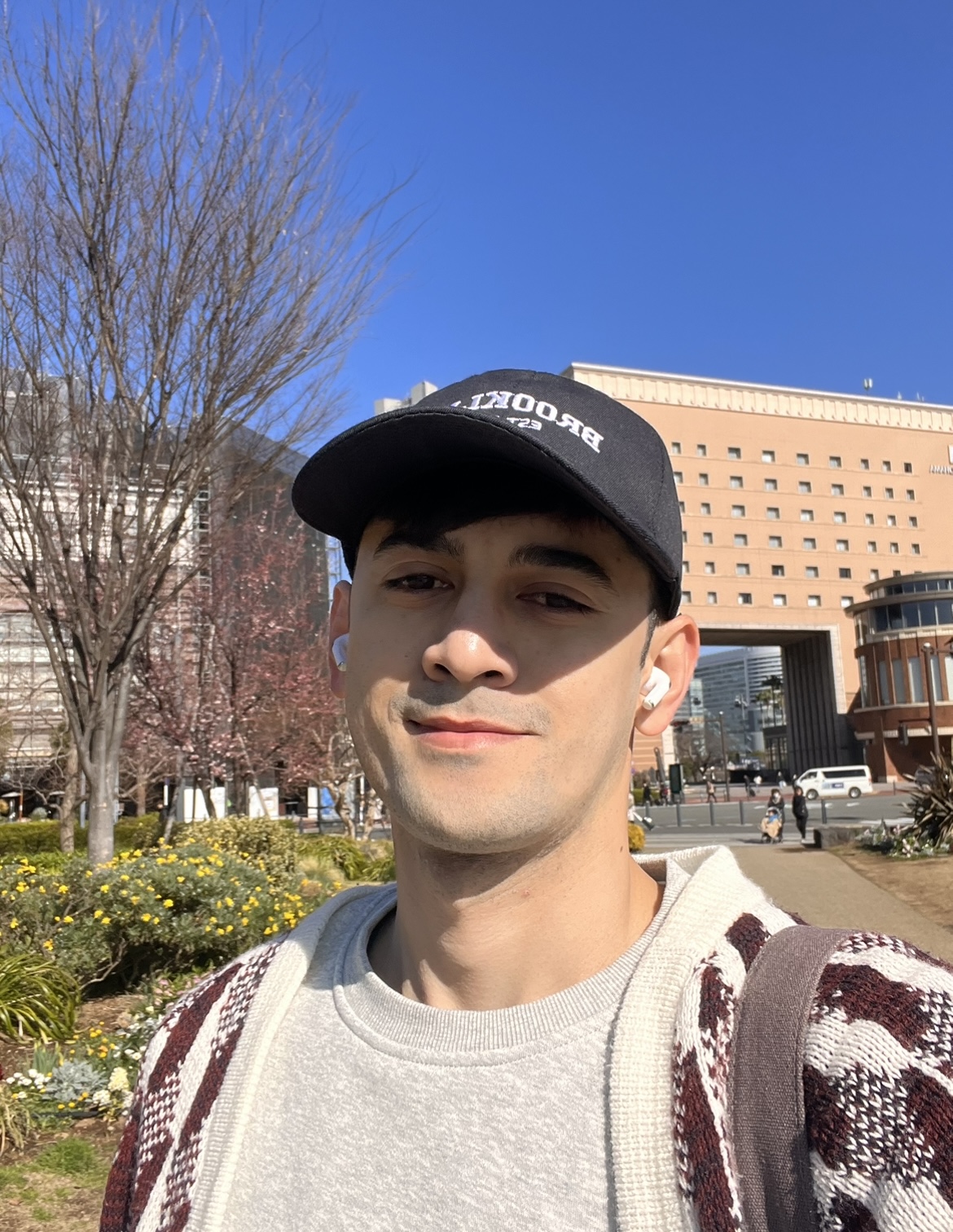 John Michael Ausejo is wearing a black cap and earbuds outdoors on a sunny day.