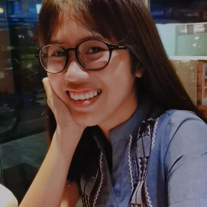 Pinoy scientist Ara Joy Pacoma has long dark hair and glasses, smileing at the camera. She rests her cheek on her hand.