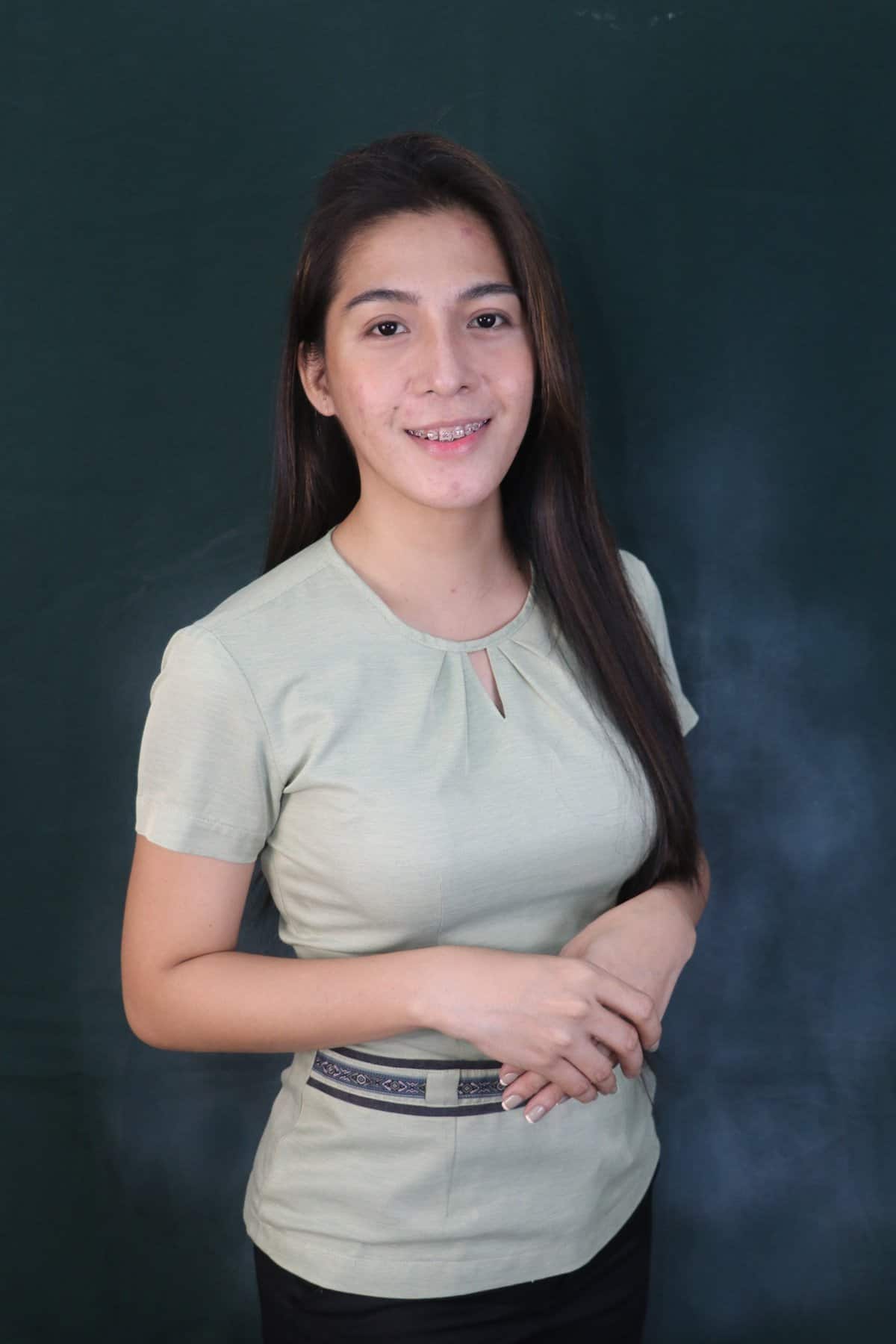 Pinoy scientist Paige Magtaan has long dark hair, wearing a light green blouse and black pants, smiling with her hands clasped in front of her.