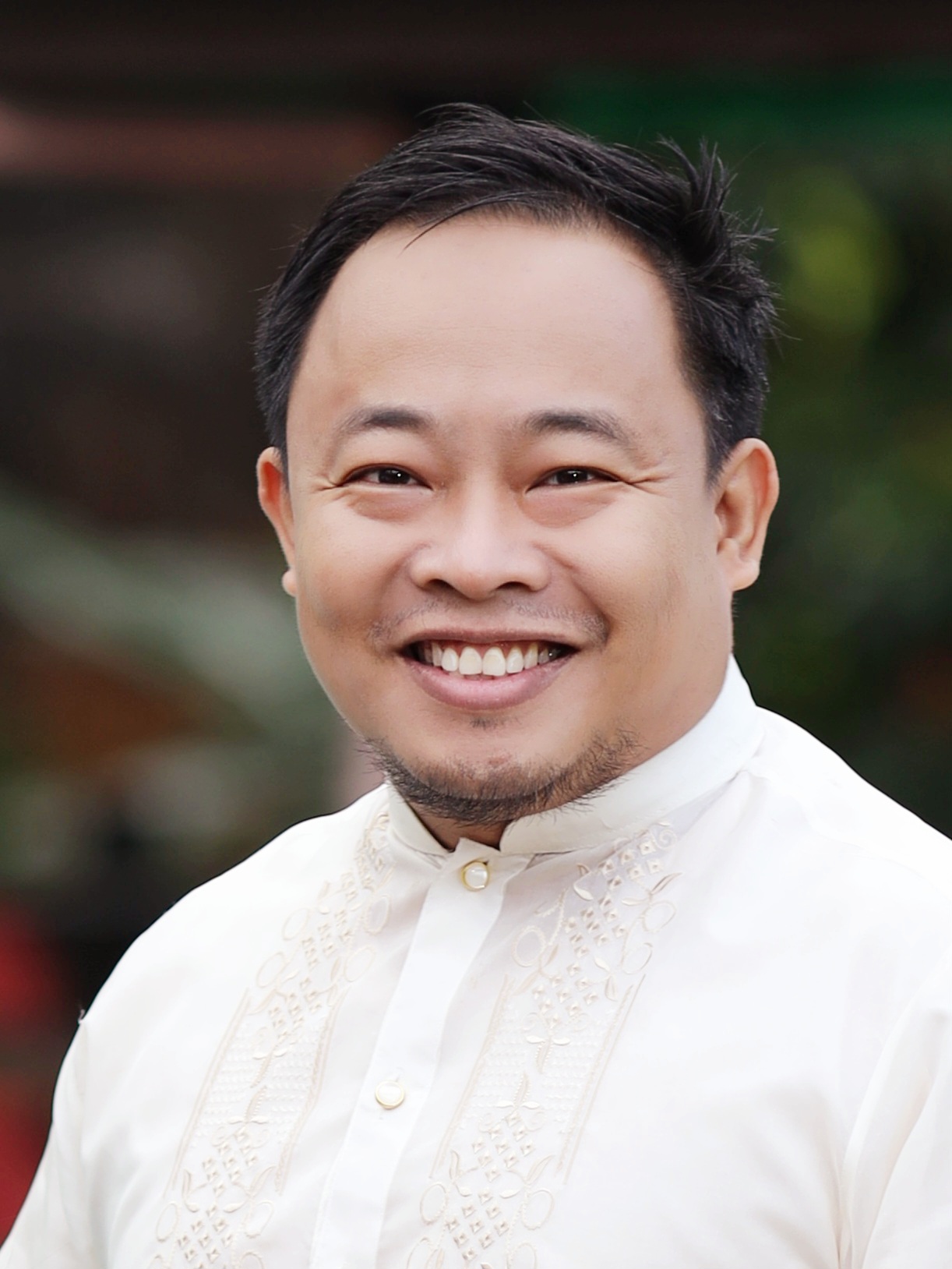 Dr. Ernest Macalalad has short black hair and a goatee, smiles at the camera while wearing a traditional white embroidered barong tagalog shirt.