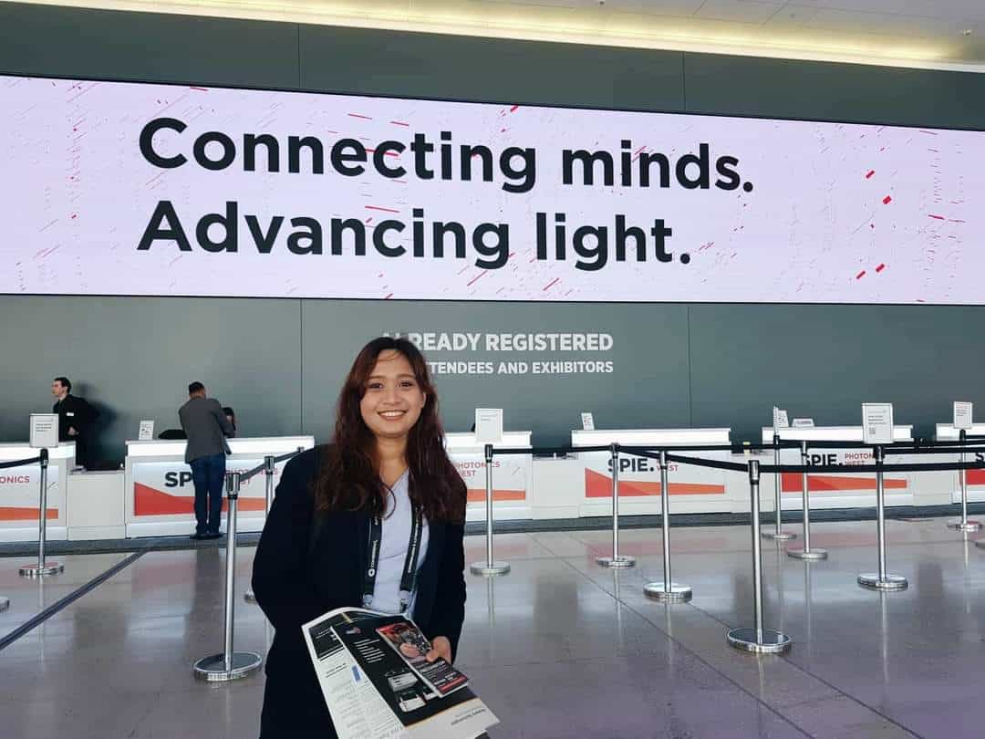 Pinoy scientist Phoebe Nicole Perez stands smiling in front of a registration area at an event