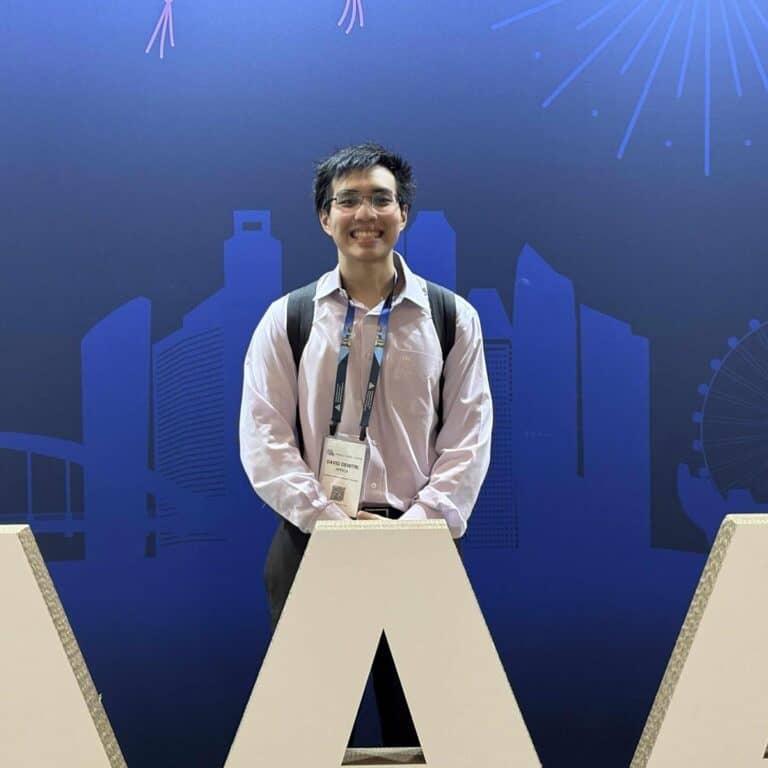 Pinoy scientist David Africa has glasses and a backpack, stands smiling in front of a blue backdrop.