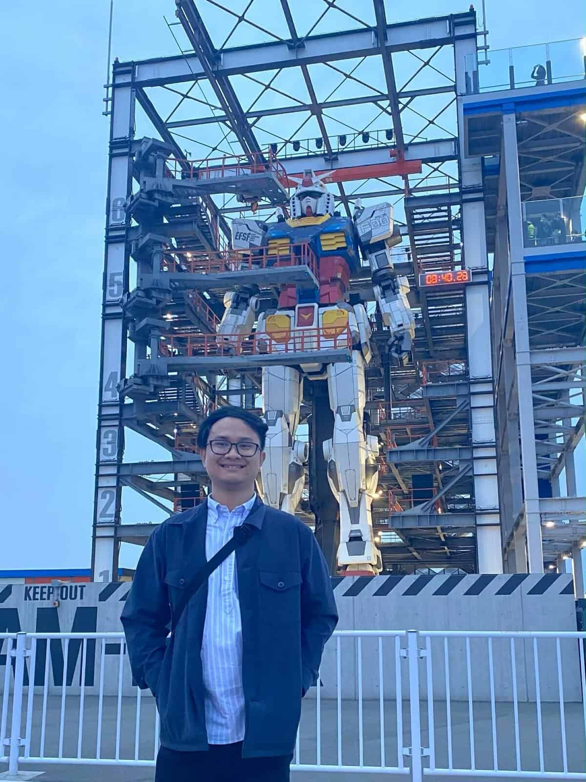Pinoy scientist Patrick De Vera stands smiling in front of a large Gundam robot statue
