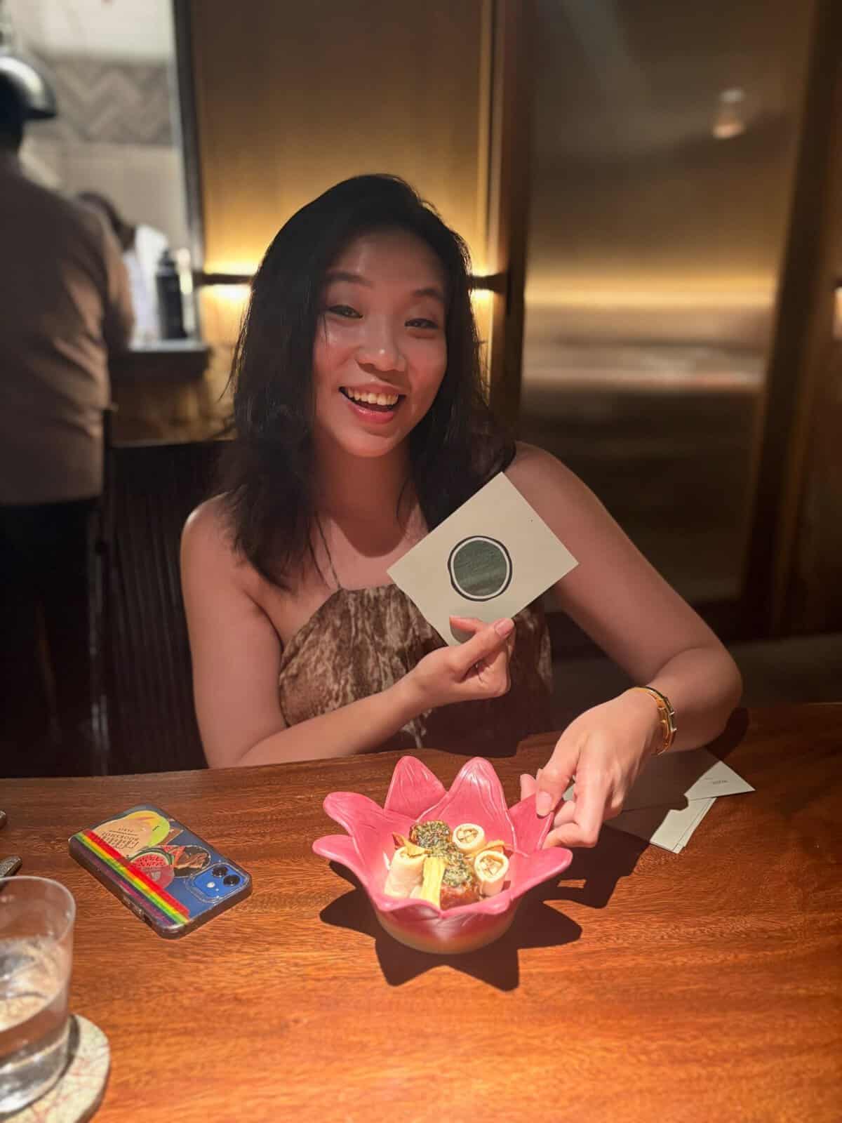 Pinoy scientist Margaret Jane Go smiling, holding a card and pointing at a dessert in a pink dish.