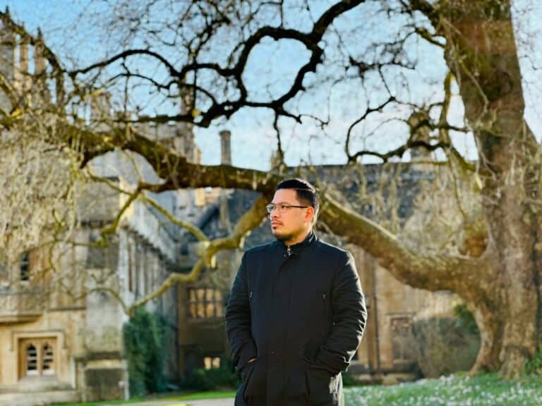 Pinoy scientist Fitz Gerald Silao in a black coat, stands outside, with bare trees and an old building in the background.