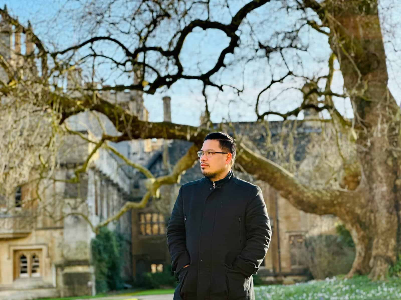 Pinoy scientist Fitz Gerald Silao in a black coat, stands outside, with bare trees and an old building in the background.
