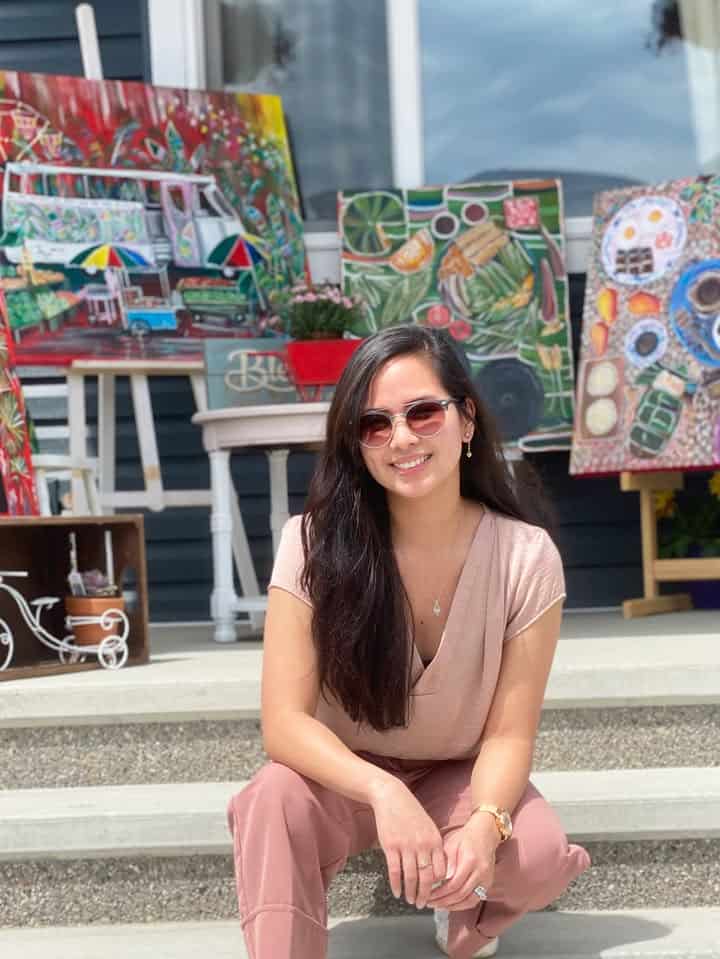Pinoy scientist Jan Elaine Soriano in pink poses on steps with colorful paintings displayed behind her.