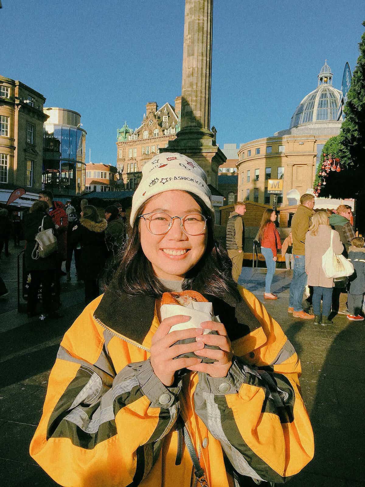 Pinoy scientist Jariel Naomi Bacar in yellow jacket smiles holding a drink in a busy sunny city square
