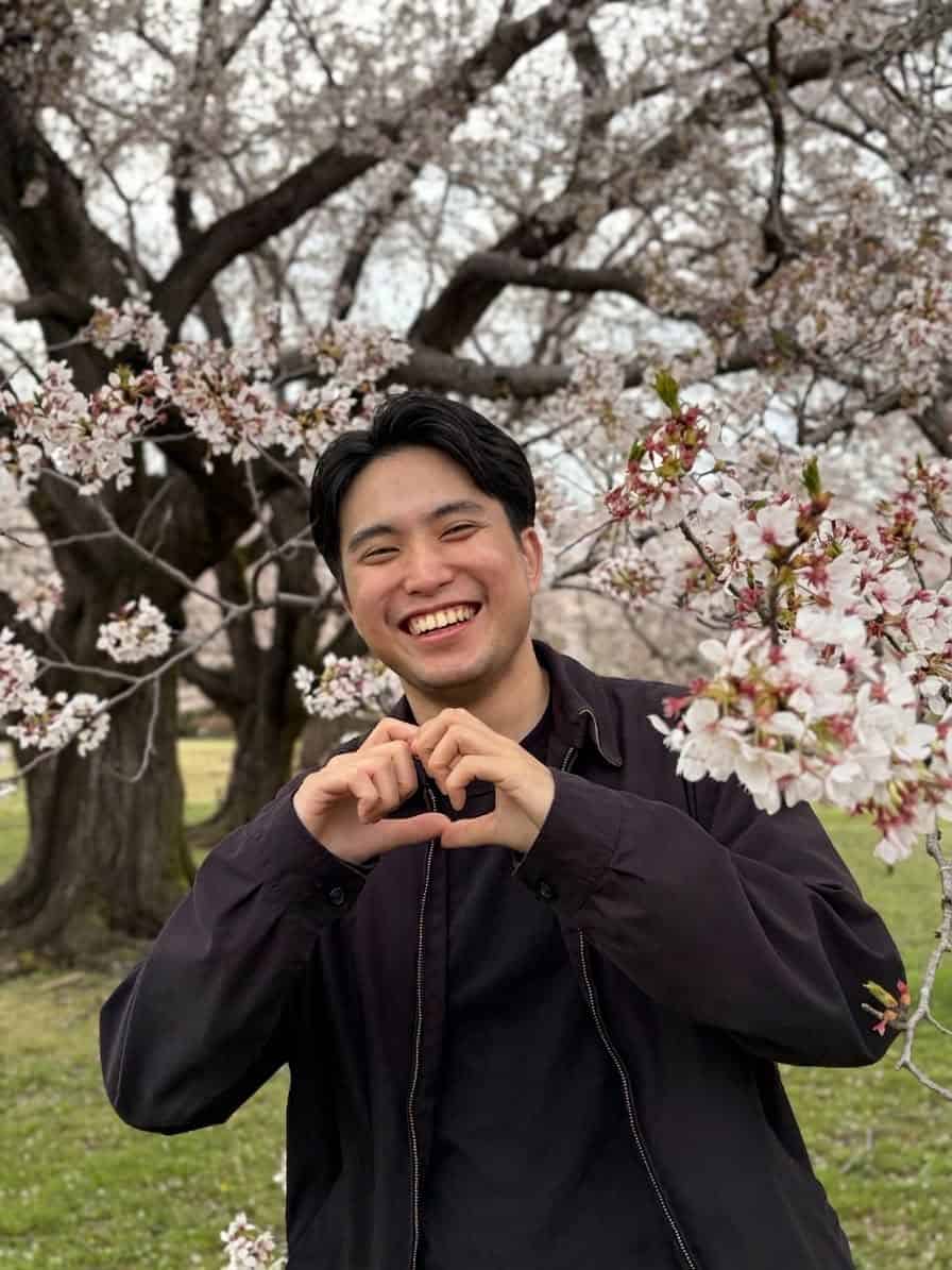 Pinoy scientist Lianne Angelico Depante smiling and making a heart sign with hands amid blooming cherry blossom trees.