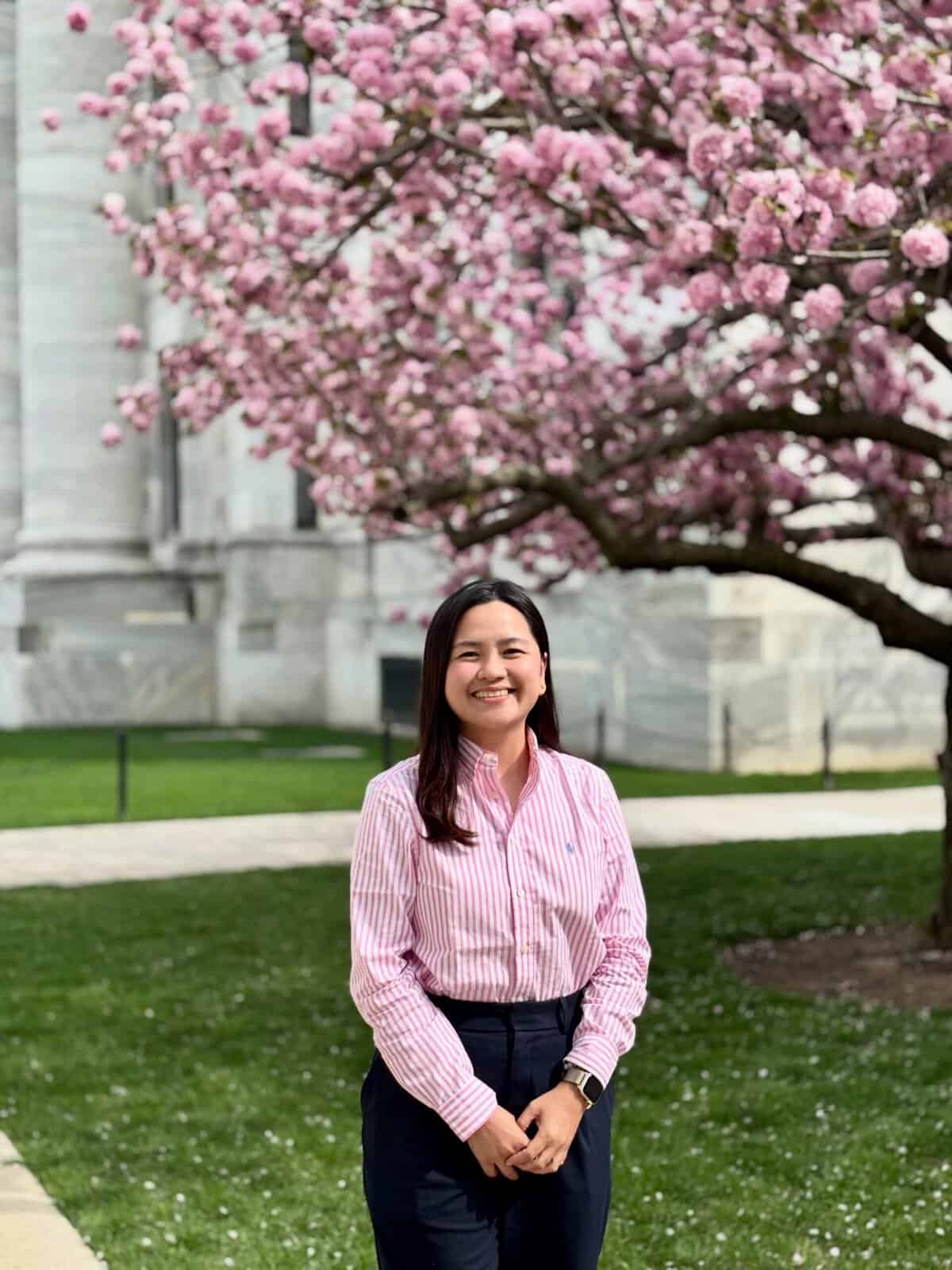 Pinoy scientist Criselle Angeline Pe&ntilde;amante in a pink striped shirt stands in front of a blooming cherry blossom tree.